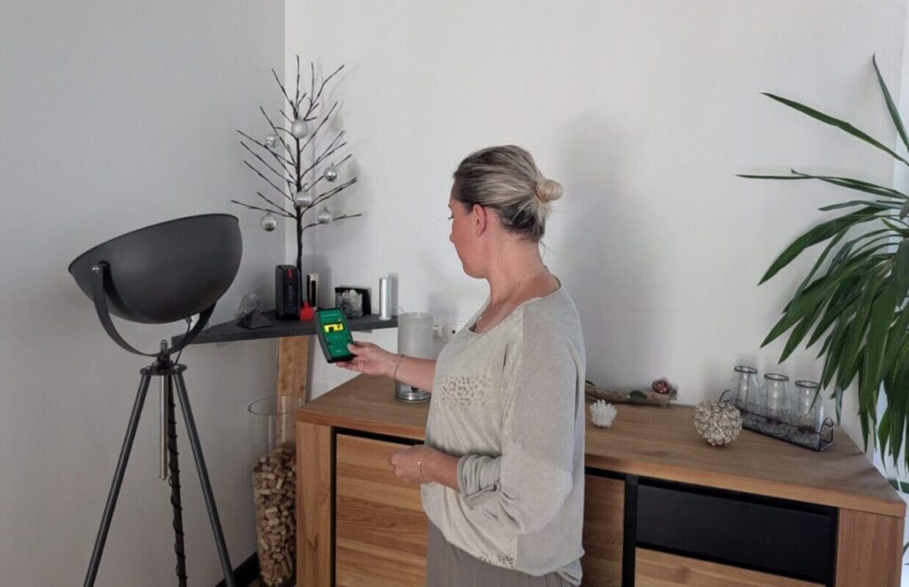 Amandine Rolland est en train de mesurer les ondes électromagnétiques hautes fréquences dans le salon d’une maison à l’aide d’un appareil professionnel Safe and Sound Pro 2.